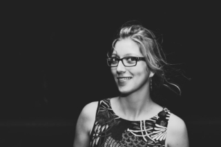 Black and white photo of a young tied hair woman wearing glasses, long earrings and smiling at the camera.