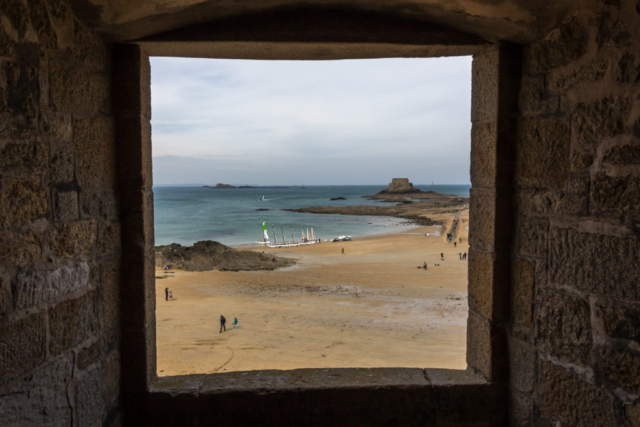 Photo of a window where we see the sea, sailing ships and rock
