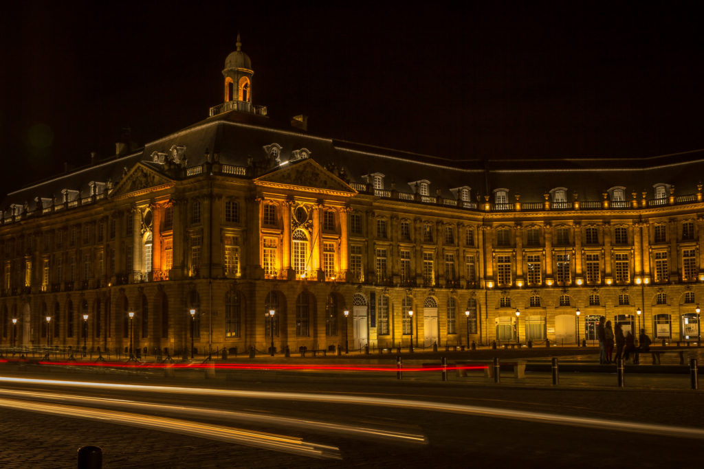 Night photo of Place de la Bourse in Bordeaux, France. Illuminated building. Red and yellow car lights in the foreground because of the long exposure.